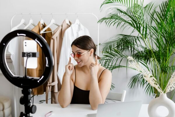 Stylish woman vlogging with ring light, surrounded by fashion accessories and greenery.